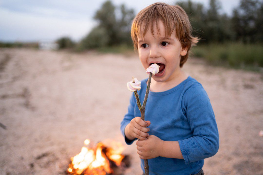 Child eating a toasted marshmallow with fire burning behind.